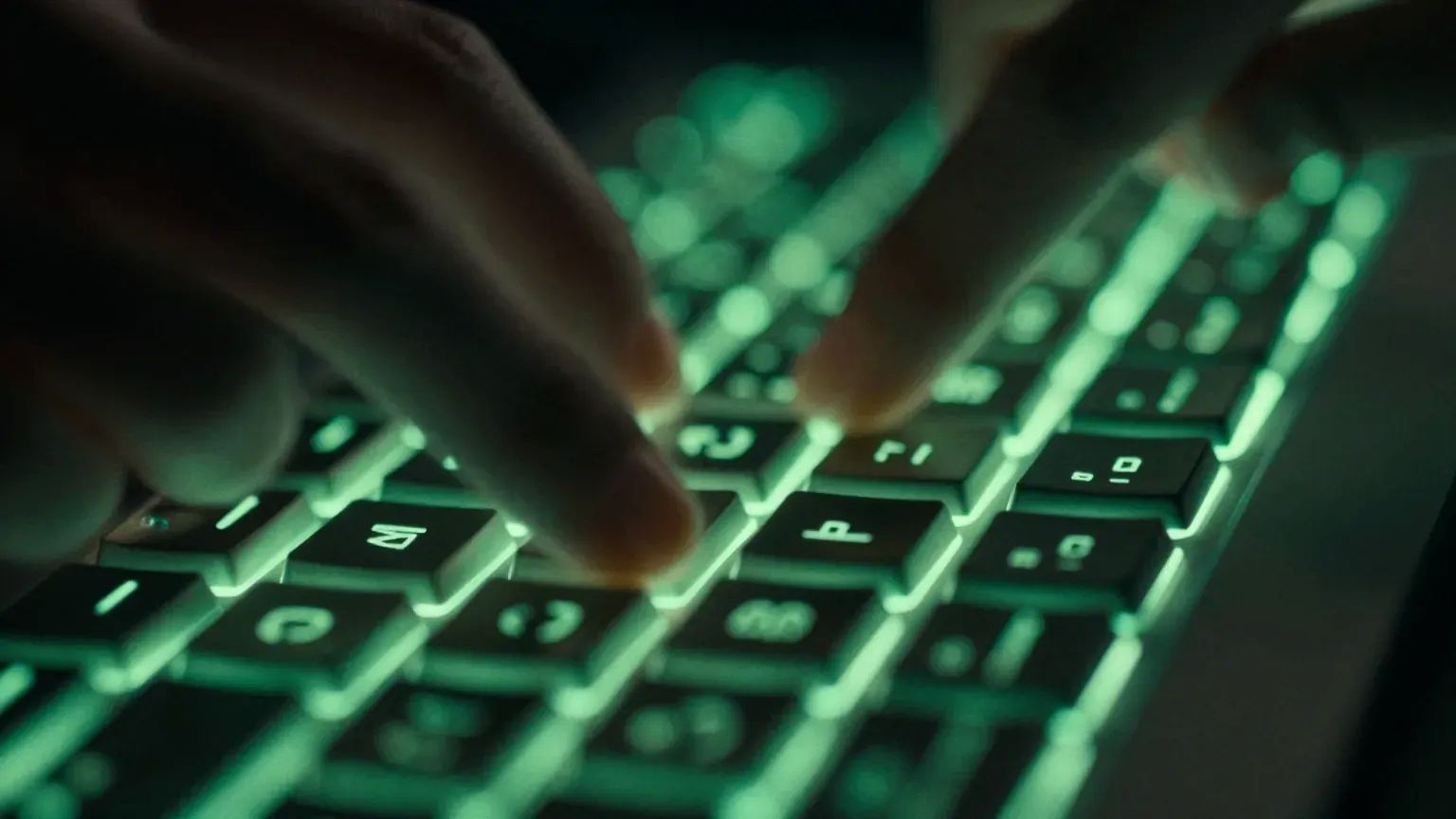Close-up of fingers striking a keyboard backlit in green